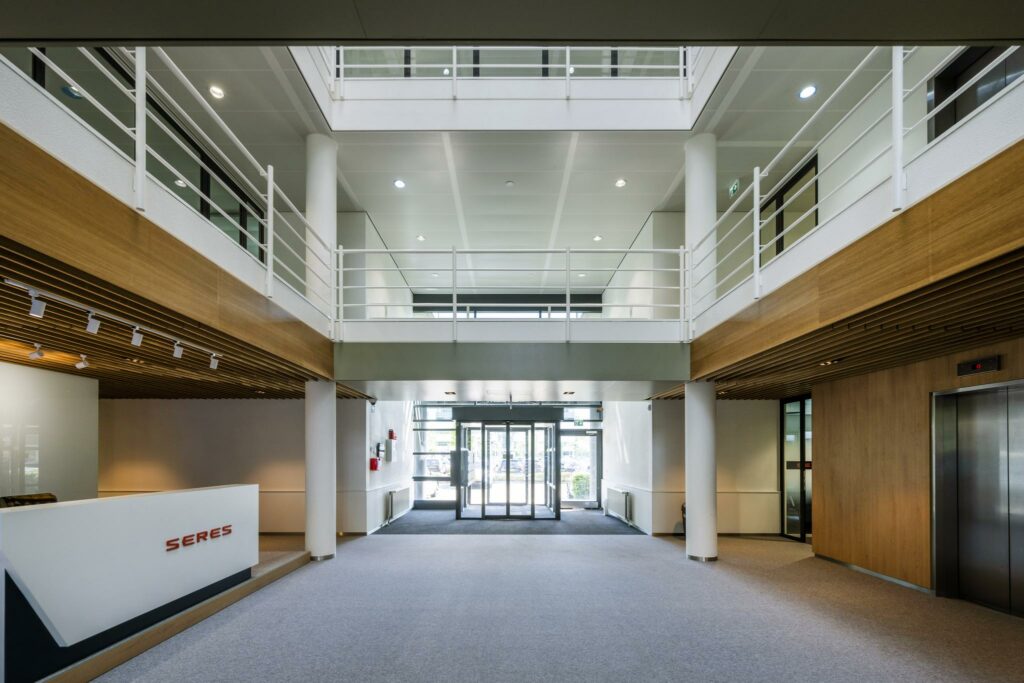 Moderne entreehal van een kantoorgebouw aan de Burgemeester Stramanweg met receptiebalie van SERES en glazen schuifdeuren.